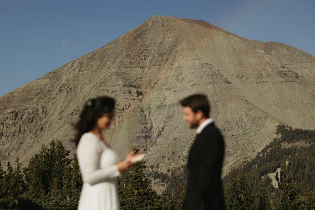 A rainbow appears in front of a mountain as a couple exchanges wedding vows.