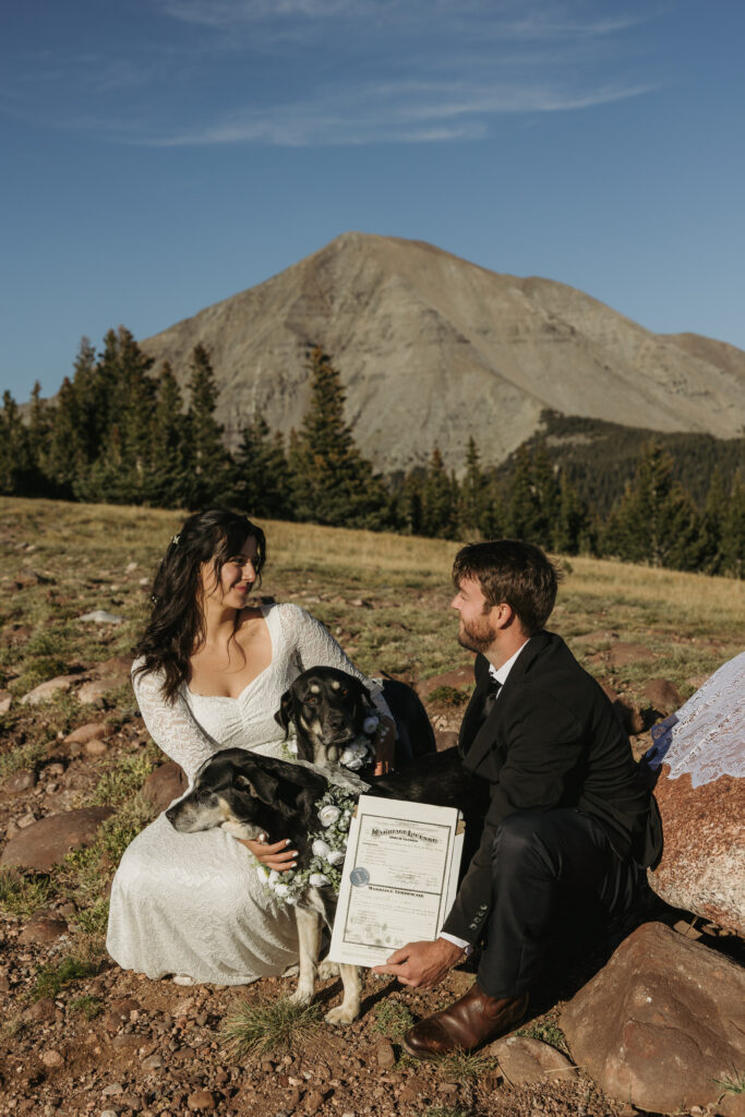 A couple looks at each other lovingly with their dogs in between them after their dogs put paw prints on their marriage license.