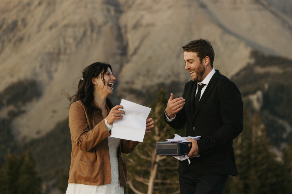 A couple laughs while reading a letter from family at their elopement day on a mountain overlook.