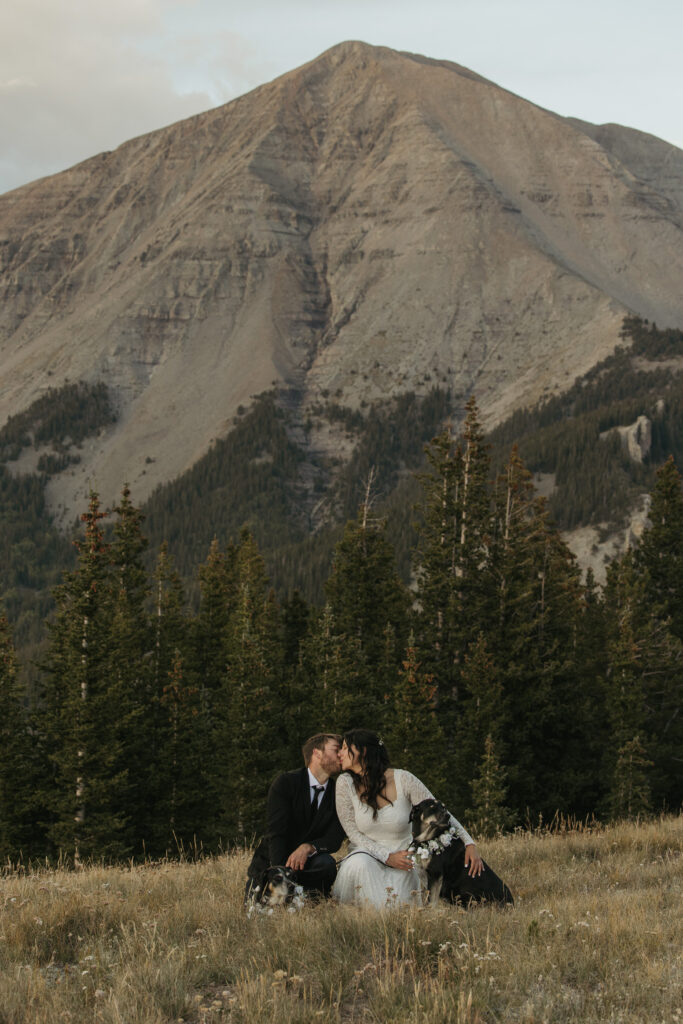 A couple kisses while posing with their dogs on their elopement day in front of West Spanish Peak.
