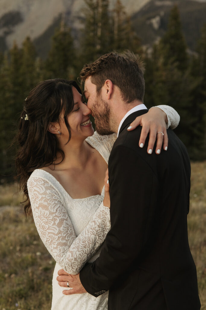 A couple smiles just before they kiss in their wedding attire on a mountain overlook.