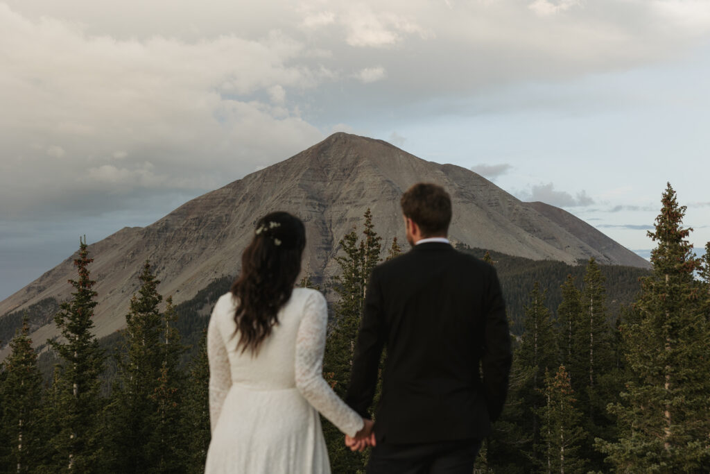 An eloping couple holds hands while facing away looking at West Spanish Peak in Colorado.